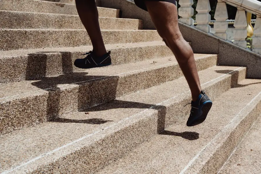 Gros plan sur les mollets d'un coureur qui monte des marches en pierre, muscles sollicités à chaque appui