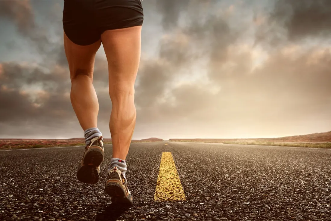 Jambes d'une coureuse en pleine foulée sur une route, illustrant la phase d'appui sur une seule jambe